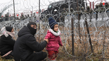 Familie de migranți la graniță în fața sârmei ghimpate și a soldaților