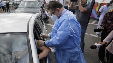 alexandru rafila in combinezon bleu cu masca vaccineaza pe cineva aflat in masina