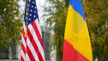 Shallow depth of field (selective focus) image with the US and Romanian flags on poles on a vegetal background.