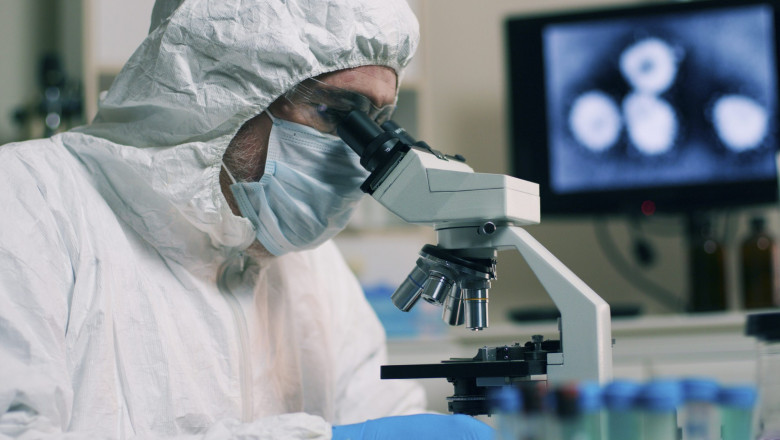Un cercetător în laborator privește la microscop.