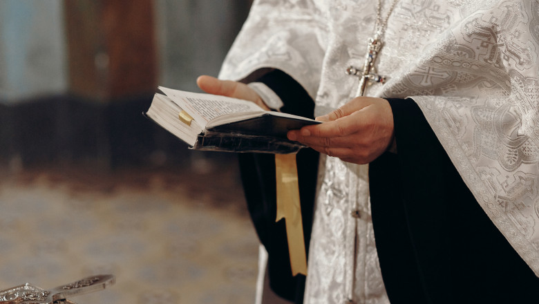 preot ortodox cu sutana citeste o carte de rugaciuni