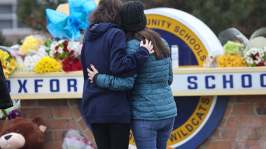 Florri pentru victimeele atacului armat de la Liceul OXford din Michigan, doua femei se imbratiseaza in fata siglei liceului