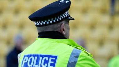 politist scotian cu vesta reflectorizanta si chipiu vazut din spate