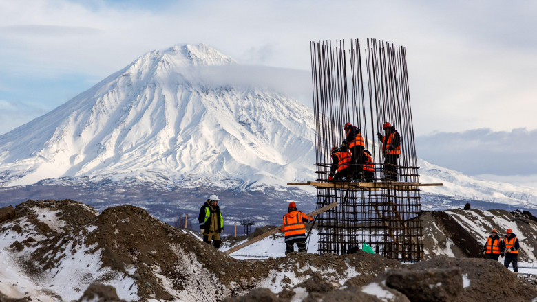 muncitori lucreaza pe un santier de constructii cu bare de metal si un munte alb pe fundal