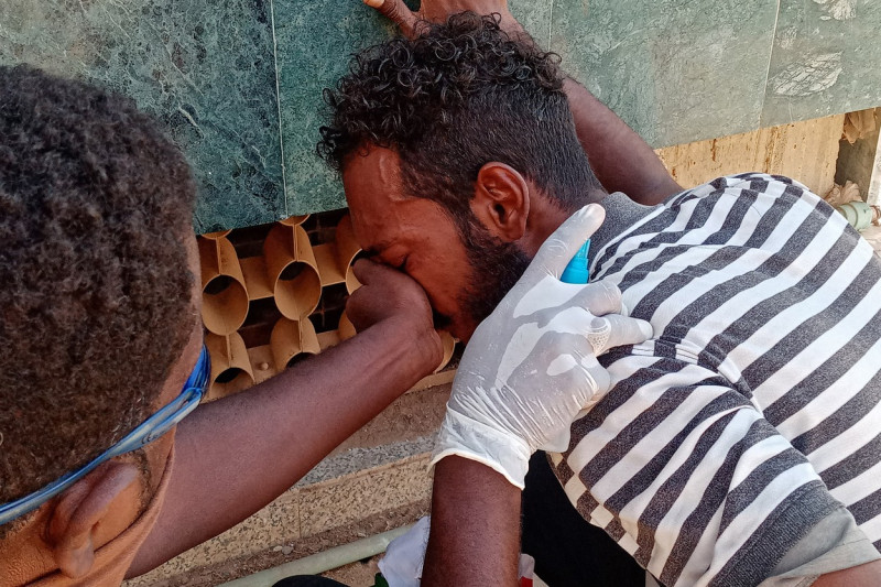 Un bărbat îi acoperă fața altuia din cauza gazelor lacrimogene la protestele din Sudan