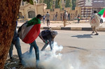 un protestatar încearcă să ridice de pe jos o grenadă de gaz lacrimogen