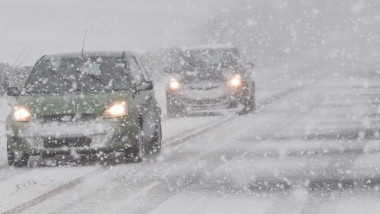 Mașini pe un drum, în ninsoare puternică.