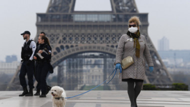 O femeie care poartă mască plimbă un cîțel în Paris.