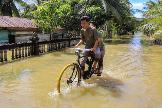 Doi bărbați pe o bicicletă prin apă inundații indonezia