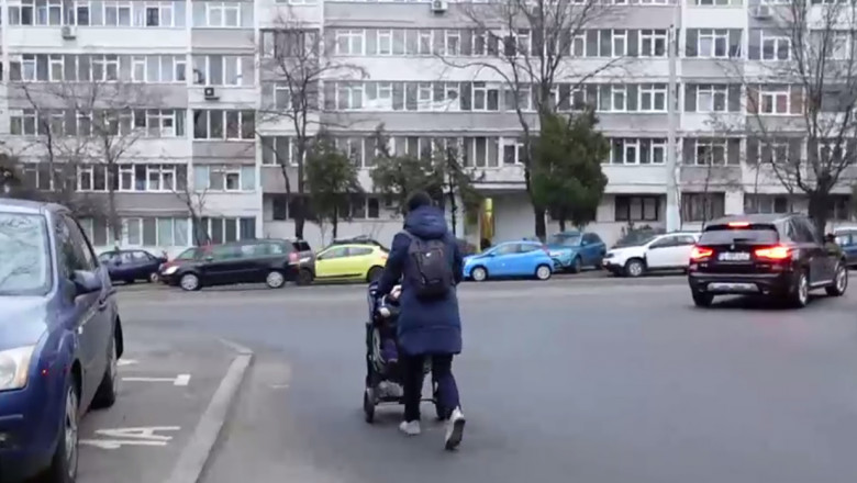 O femeie cu cărucior merge pe stradă din cauza mașinilor parcate pe trotuar.