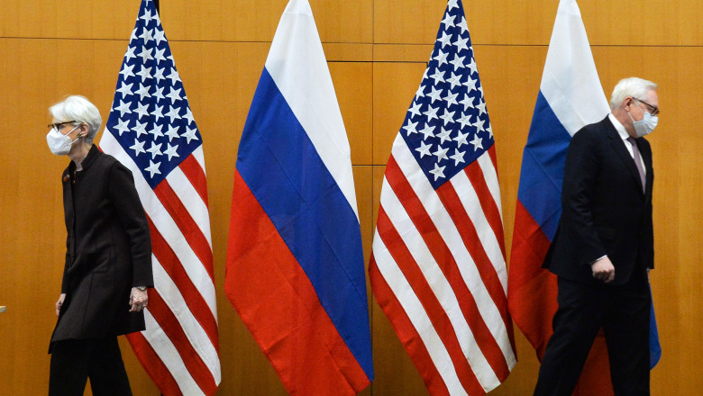 Secretarul adjunct de stat american Wendy Sherman și vice-ministrul rus de externe, Serghei Ribakov, la negocierile de la Geneva, cu masti pe gigura si steaguri pe fundal, se uita in directii opuse