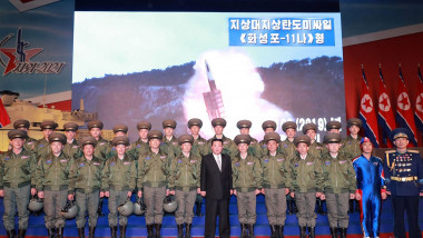 Kim Jong-un pozează cu mai mulți militari în fața unui ecran în care e redată testarea unei rachete balistice