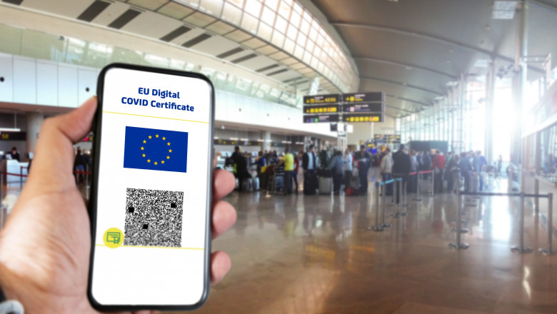 EU Digital COVID Certificate with the QR code on the screen of a mobile held by a hand with blurred airport in the background