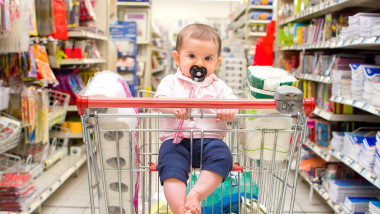 copil cu suzeta in cosul de cumparaturi la supermarket