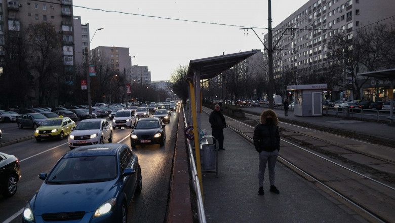 oameni asteapta in statie tramvai, multe masini pe strada