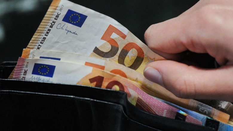 O persoană scoate o bancnotă de euro din portofel.