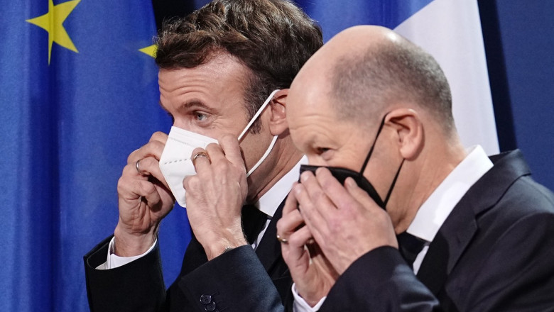 Emmanuel Macron și Olaf Scholz isi aranjeaza mastile de protectie inainte de o conferinta de presa