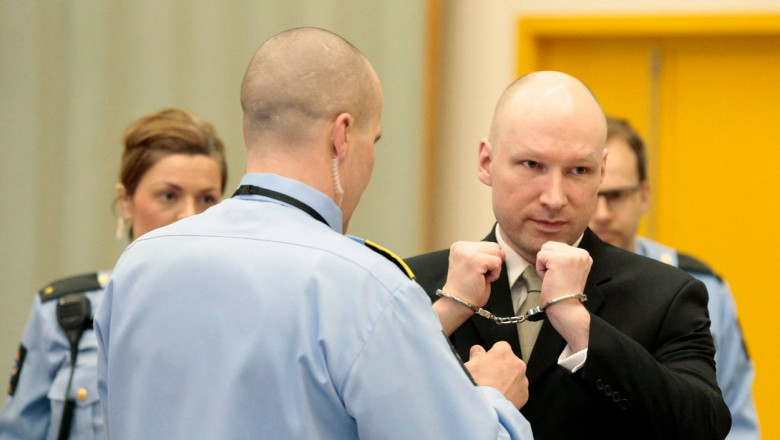 Anders Breivik cu cătușele la mâini stă în fața unui polițist
