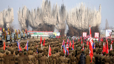militari aliniati cu steaguri in fundal avand explozii care inaugureaza un santier