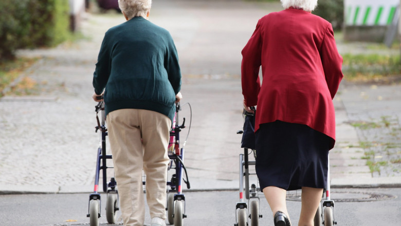 Două femei în vârstă se deplasează cu ajutorul unor cărucioare.