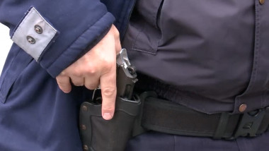 Un polițist cu mâna pe pistolul aflat în toc.