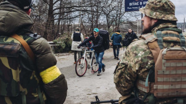 A young man walks, next to his bike, as two Ukrainian soldiers watch him, March 5, 2022, in Irpin, Ukraine.