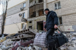 Bărbat cu sacoșe în mâini printre ruinele unui bloc distrus de bombardamente