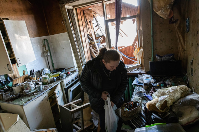 femeie caută printre dărâmături și bunuri distruse