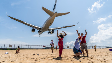 turisti pe o plaja din thailanda in itmp ce un avion se pregateste de aterizare
