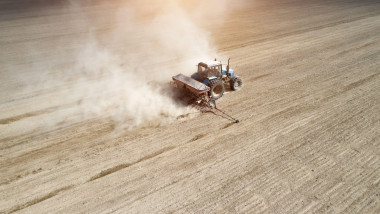 Aerial view of tractor with mounted seeder performing direct seeding of crops on plowed agricultural field. Farmer is using farming machinery for plan