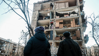 doi oameni privesc un bloc cu peretele vertical spulberat de bombardament