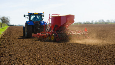 Farm tractor and seed drill sowing ploughed field in spring