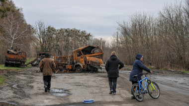 civili in ucraina merg pe un drum cu vehicule distruse