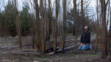A Ukrainian man named Maxim prays next to a dead male with his hands bound at an abandoned Russian camp near Makariv, Ukraine