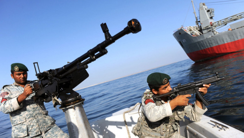 2 marinari iranieni cu mitraliere in barca se indreapta spre o nava mare