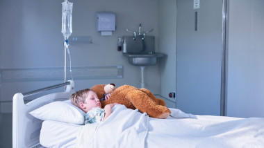 copil pe patul de spital cu un ursulet de plus in brate