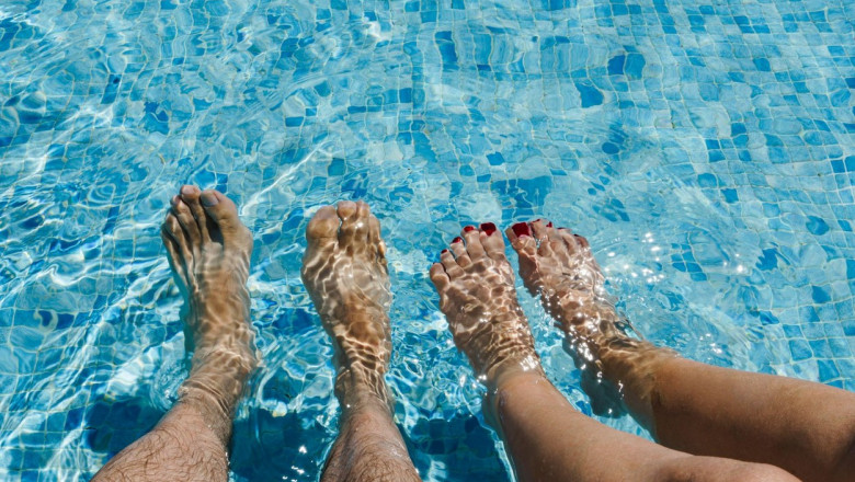 Feet of a couple of men and women, she with her nails painted red in the water of a swimming pool, with copy space in the upper part of the image.
