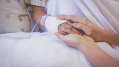 manuta unui copil bolnav cu perfuzie este tinuta in palme de un adult