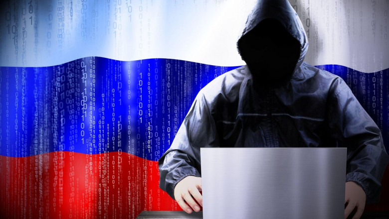 silueta hacker cu gluga si laptop, cu steagul rusiei in spate