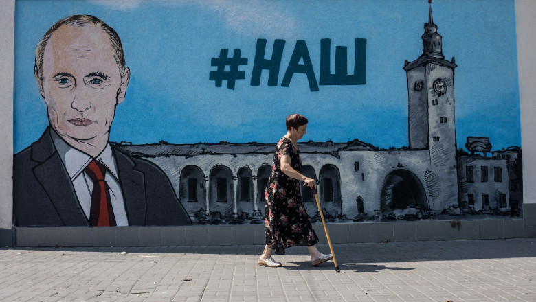 femeia cu baston trece pe langa un desen mural înfățișându-l pe Vladimir Putin în Crimeea