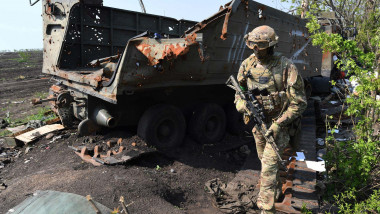 A Ukrainian soldier passes in front of a Russian armored vehicle near the trenches in the village of Malaya Rohan