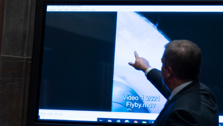 bărbat arată cu degetul spre un ecran pe care rulează un clip video