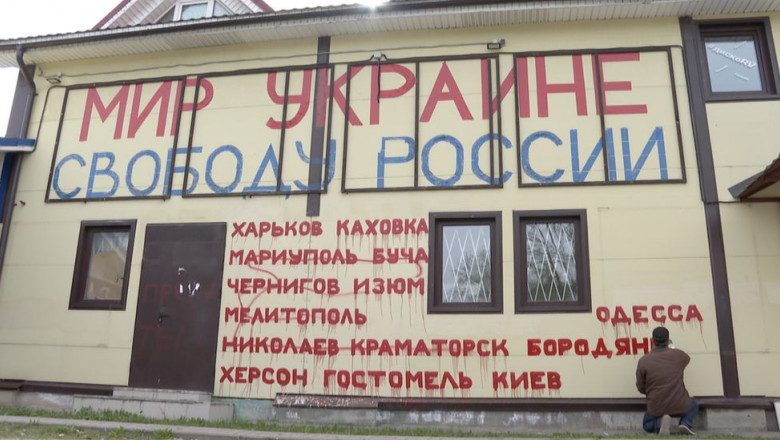 un rus scrie cu vopsea numele localitatilor bombardate