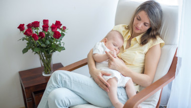 Young mother holding her baby, rocking him to sleep, sitting in armchair