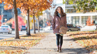 Young happy woman on sidewalk street walking in Washington DC, USA United States in alley of golden orange yellow foliage autumn fall trees on road during sunny day