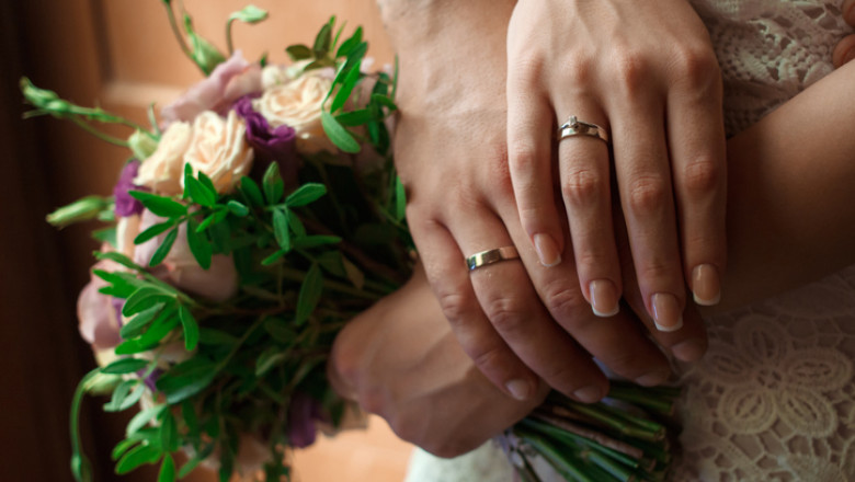 hands of the bride and groom with wedding rings, bride holds a wedding bouquet in hands, the groom hugs her from behind