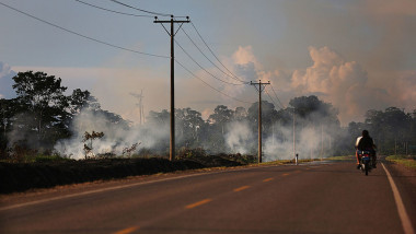 motociclist pe un drum pustiu, acoperit parțial de fum produs de incendiu de vegetație, imagine apocalipsa meteo, schimbări climatice