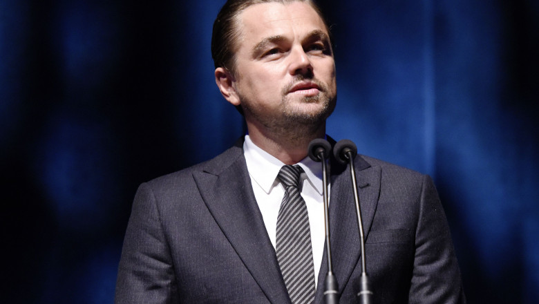 Leonardo DiCaprio priveste in sus cu spatele la un fond albastru