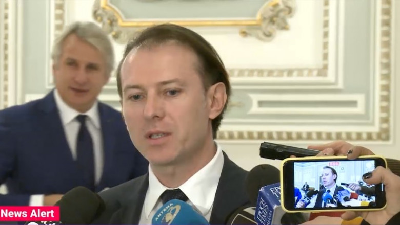 Eugen Teodorovici trece prin spatele ministrului Florin Cîțu în timp ce acesta face declarații jurnaliștilor și îi strigă câteva cuvinte