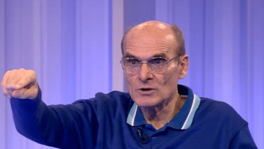 Cristian Tudor Popescu cu ochelari si tricou albastru gesticuleaza cu mana intinsa